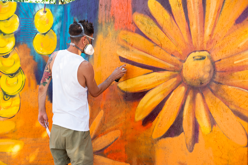Male graffiti artist using spray for a large mural with floral elements